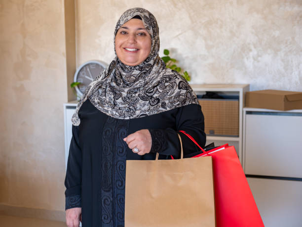 mulher árabe segurando sacos de compras dentro de casa - women holding shopping bag living room - fotografias e filmes do acervo