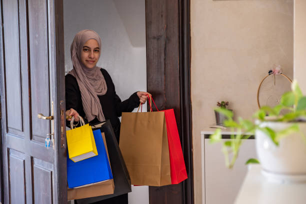 mulher árabe do oriente médio da jordânia segurando sacolas de compras e entrando em casa com sorriso no rosto usando hijab e abaya - women holding shopping bag living room - fotografias e filmes do acervo