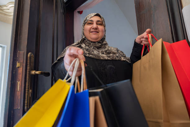 mulher árabe do oriente médio da jordânia segurando sacolas de compras e entrando em casa com sorriso no rosto usando hijab e abaya - women holding shopping bag living room - fotografias e filmes do acervo