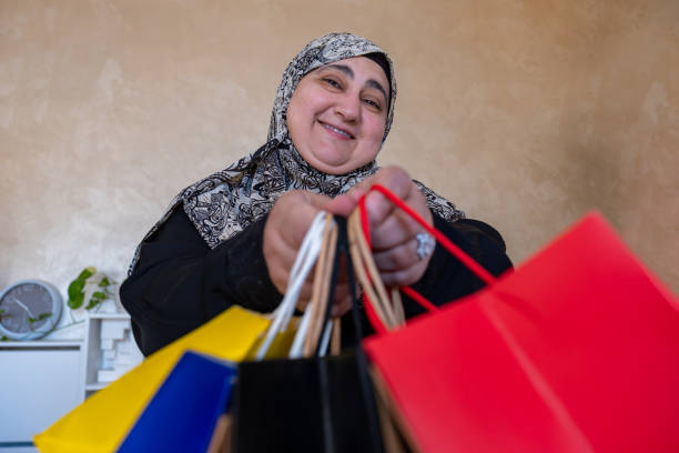 mulher árabe vestindo abaya segurando saco de compras dentro de casa na sala de estar e sorrindo - women holding shopping bag living room - fotografias e filmes do acervo