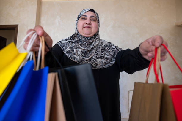 mulher árabe vestindo abaya segurando saco de compras dentro de casa na sala de estar e sorrindo - women holding shopping bag living room - fotografias e filmes do acervo