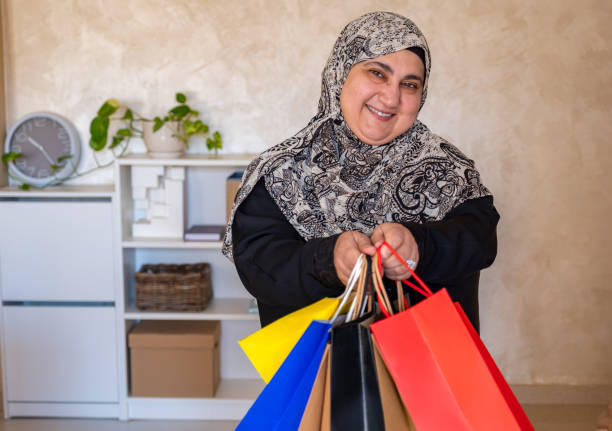 mulher árabe vestindo abaya segurando saco de compras dentro de casa na sala de estar e sorrindo - women holding shopping bag living room - fotografias e filmes do acervo