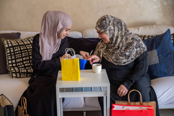 mulher árabe na sala de estar com sua mãe verificando sacolas de compras após as compras e fornecendo presente para sua mãe - women holding shopping bag living room - fotografias e filmes do acervo