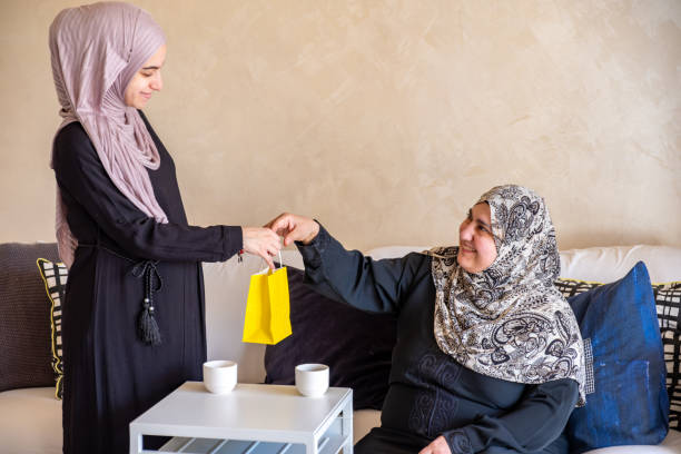 mulher árabe na sala de estar com sua mãe verificando sacolas de compras após as compras e fornecendo presente para sua mãe - women holding shopping bag living room - fotografias e filmes do acervo