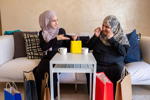 mulher árabe na sala de estar com sua mãe verificando sacolas de compras após as compras e fornecendo presente para sua mãe - women holding shopping bag living room - fotografias e filmes do acervo