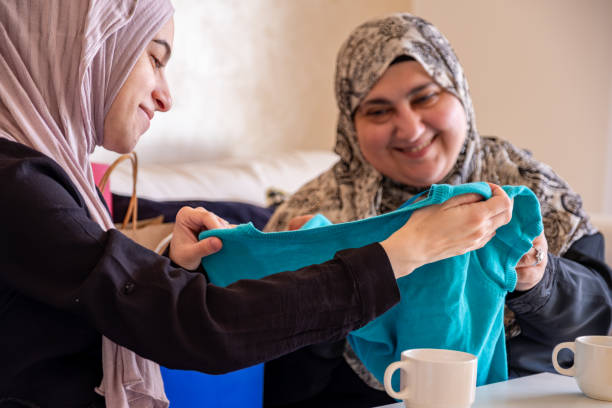 mulher árabe presenteando sua mãe e mostrando as roupas novas depois de fazer compras com sacolas de compras ao fundo na sala de estar - women holding shopping bag living room - fotografias e filmes do acervo