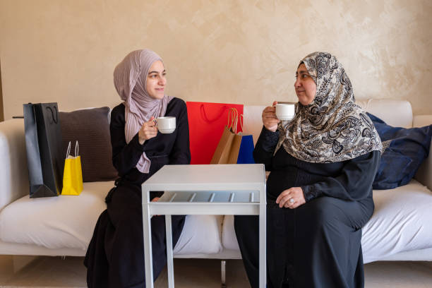 mulheres árabes usando hijab gostam de beber café na sala de estar juntas descansando após as compras - women holding shopping bag living room - fotografias e filmes do acervo