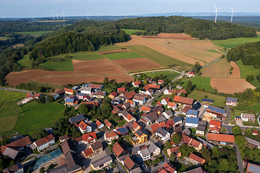 A village among agricultural fields and forests. Wind turbines are visible on the horizon.