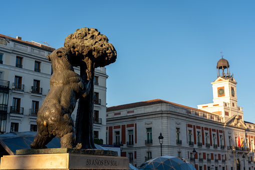 The bear and the strawberry tree in Puerta del Sol square and tower with clock in the background. Madrid. Spain. July 29, 2023.