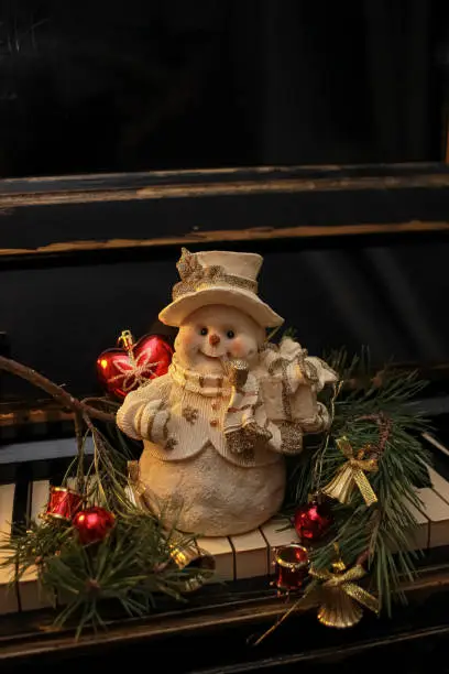 Photo of Decorative figurine of a snowman with a Christmas tree on a old shabby piano. Festive new year decor, warm dark composition