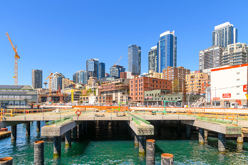 Construction cranes and work being done on the downtown Seattle Waterfront and cruise port along Alaska Way, with the city skyline and aquarium in view in Seattle Washington, USA.