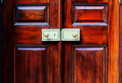 Close-up of two closed antique exterior red wood doors with pronounced grain. A pair of metal locks in the center.