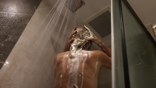 Woman rinses foam from hair under running water in shower