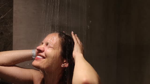 Smiling woman washes body under running water in shower