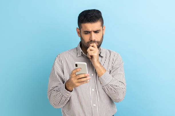 Man holding chin with smartphone in hand, contemplating about software updating, choosing tariffs. stock photo