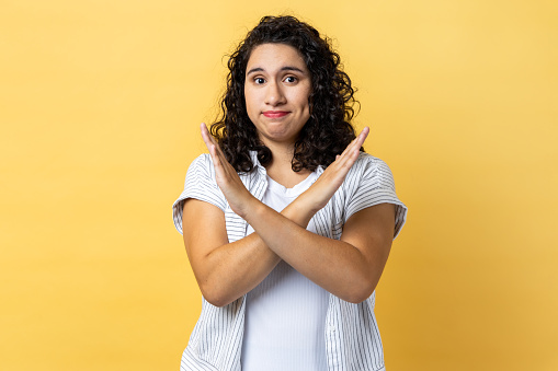 No way, this is finish. Portrait of woman with dark wavy hair gesturing stop, x sign with crossed hands, way prohibited, warning of troubles. Indoor studio shot isolated on yellow background.