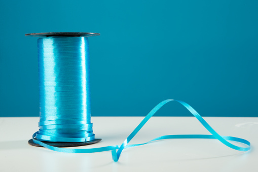 Blue ribbon spool on white table against blue background