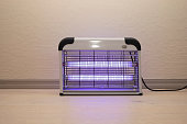 Electric Mosquito and Insect Zapper With Blue Purple Lights Turned on. Bug Killer Lamp on Wooden Floor in Room. Fly Trap for Outdoor and Indoor. Horizontal Plane