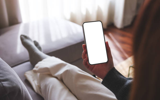 istock Mockup image of a woman holding mobile phone with blank desktop white screen while lying on a sofa at home 1739955485