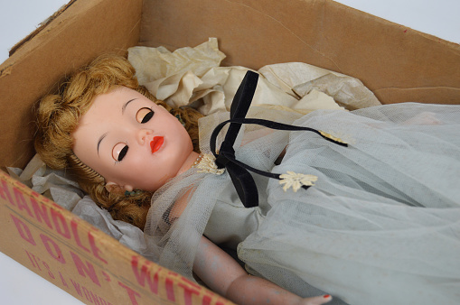 Old doll sleeping in a cardboard box.