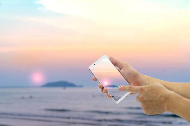 hand holding mobile smart phone with front the beach and sky  background