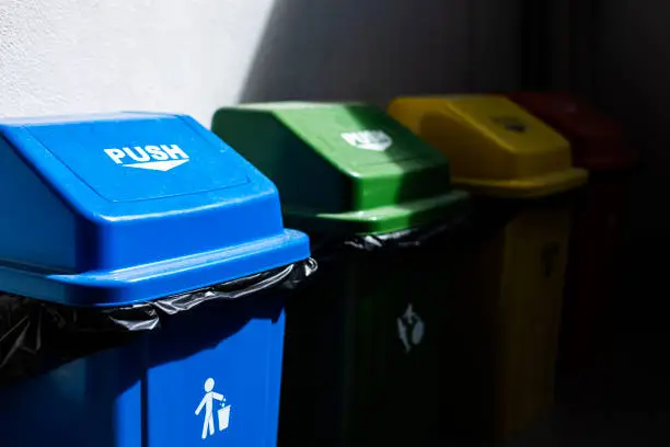 Multicolored Garbage Trash Bins. Recycle Bin on the floor and white wall.