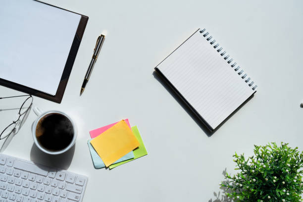 istock Top view above of white office desk table with keyboard computer, notebook and coffee cup with equipment other office supplies. business concept. workplace, flat lay with blank copy space 1740000911
