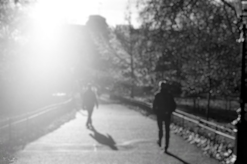 Defocused view of public park with silhouette of people in London with bright sunlight through building. Use for background template. Black and white image.