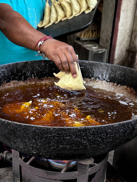 istock Close-up image of unrecognisable person placing samosas into karahi (Indian wok), bubbling hot oil, batch of samosas deep frying, Indian street food stall, unhealthy eating, focus on foreground 1740185800