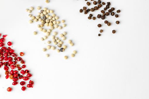 Black, red and white peppercorns scattered on white background close up