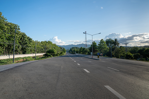 A ground-level perspective of a rural street in Tak Province, Thailand, in open sky during the day. This road serves as key transportation artery to western region of country.