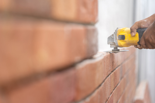 Close up to Grinder Machine in Worker man hand hold saw, grind, check and kept detailed polyurethane foam Brick wall with dust all around.