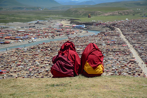 Sichuan, China - Aug 18, 2016. Tibetan monks sitting on the hill and looking at Yarchen Gar in Sichuan, China. Yarchen Gar is the largest concentration of nuns and monks in the world.