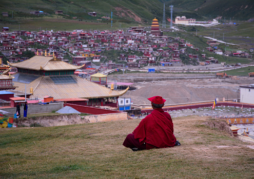 Sichuan, China - Aug 18, 2016. A Tibetan monk sitting on the hill and looking at Yarchen Gar in Sichuan, China. Yarchen Gar is the largest concentration of nuns and monks in the world.