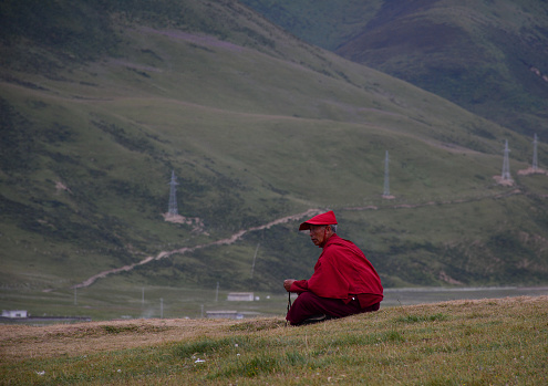 Sichuan, China - Aug 18, 2016. A Tibetan monk sitting on the hill and looking at Yarchen Gar in Sichuan, China.