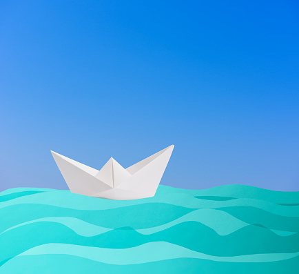 Blank origami paper boat sailing on the blue paper wave against clear sky with copy space.