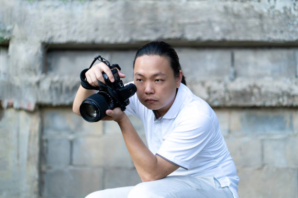 istock Professional Asian Chinese - Thai Camera man posture and focus in viewfinder and LED screen on mirrorless camera medium format in construction concrete area. 1740249534