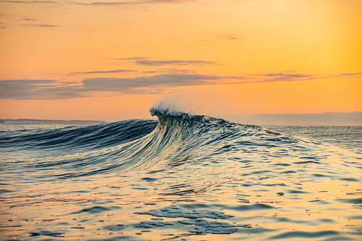 Smooth curved waves in the ocean with golden sky at dusk. Photographed on the south coast of NSW, Australia.