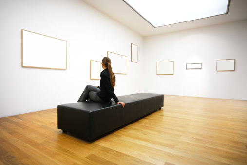 woman seating on a bench and looking at different white frames in an art gallery. 