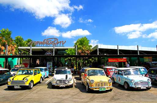 Nakhonratchasima, Thailand -  September 20, 2023: Colorful classic Mini Austin cooper parking on street in front of Thai coffee shop with building and blue sky background. Small vehicle, Vintage car