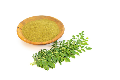 Moringa powde in a wooden bowl with fresh green leaves isolated on a white background