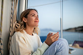 Beautiful woman enjoying morning coffee on sailboat deck on a cold autumn day an off-season vacation