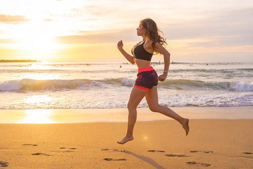 Sportive woman running along a sandy beach during sunset