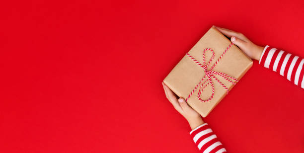 istock gift box in children's hands on a red background, presenting a gift with place for text 1740300238