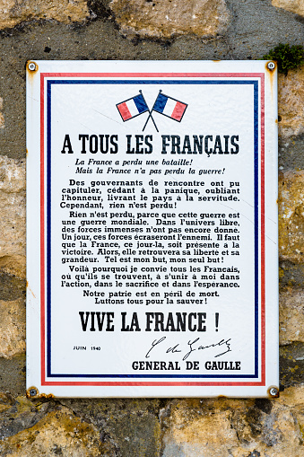 Sainte-Mère-Eglise, France - Sept. 6, 2023: Close-up of an enamel sign showing the poster A Tous Les Français by General de Gaulle, following the Appeal of 18 June 1940, screwed on a stone wall.