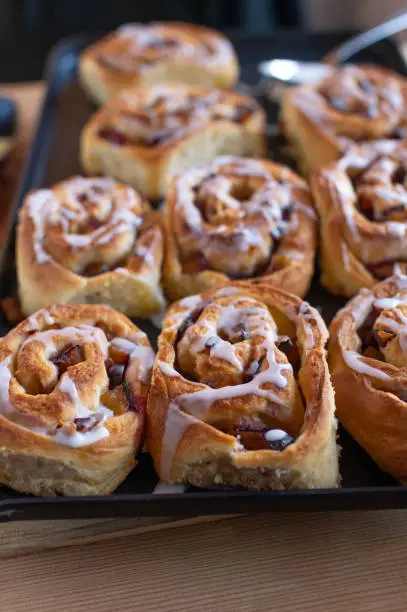 Delicious homemade german pastry with fresh baked and sticky plum, cinnamon rolls with sweet sugar glaze. Served warm and ready to eat on a baking sheet. Closeup, selective focus