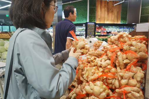 Woman choosing fresh ginger at the supermarket. Customers buying food at grocery shops.