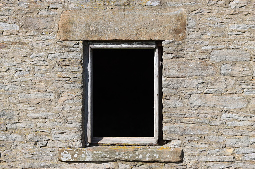 An empty window in the stone wall of an abandoned farmhouse