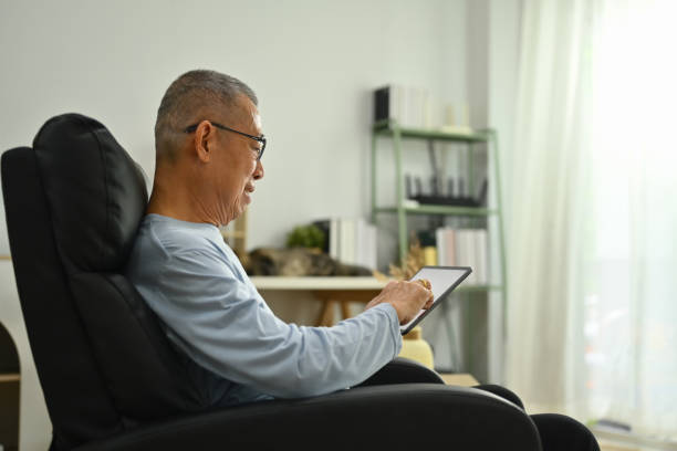 istock Side view of 70s elderly man sitting on the armchair and using digital tablet 1740345105