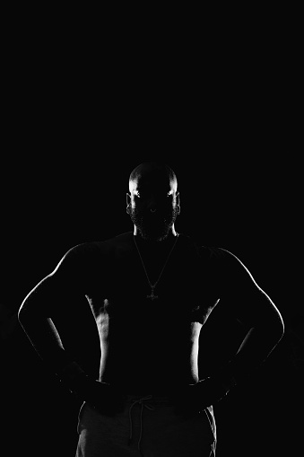 Silhouette of a muscular man with his hands on his waist in black and white in a studio shot with copy space